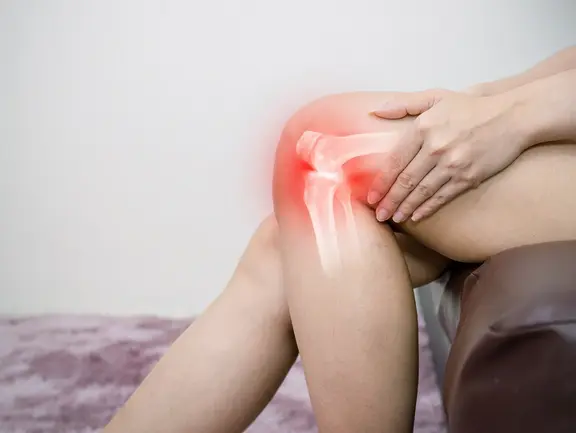 Frau hat Mühe beim Aufstehen, was die für Arthrose charakteristischen Anlaufschmerzen und Bewegungseinschränkungen symbolisiert.
