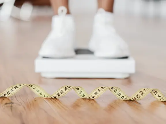 Das Risiko von Übergewicht: Die hohe Druckbelastung auf Knie und Hüfte Darstellung einer Person auf der Waage, da Übergewicht ein Risikofaktor für Arthrose ist.